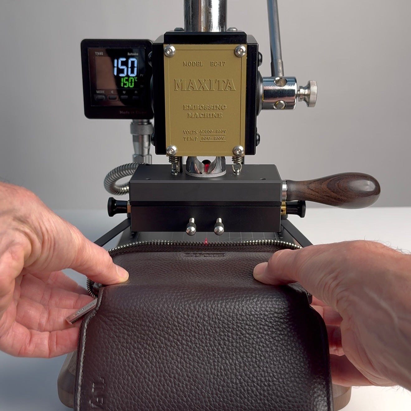Hands putting a jewellery case into a leather embossing machine.