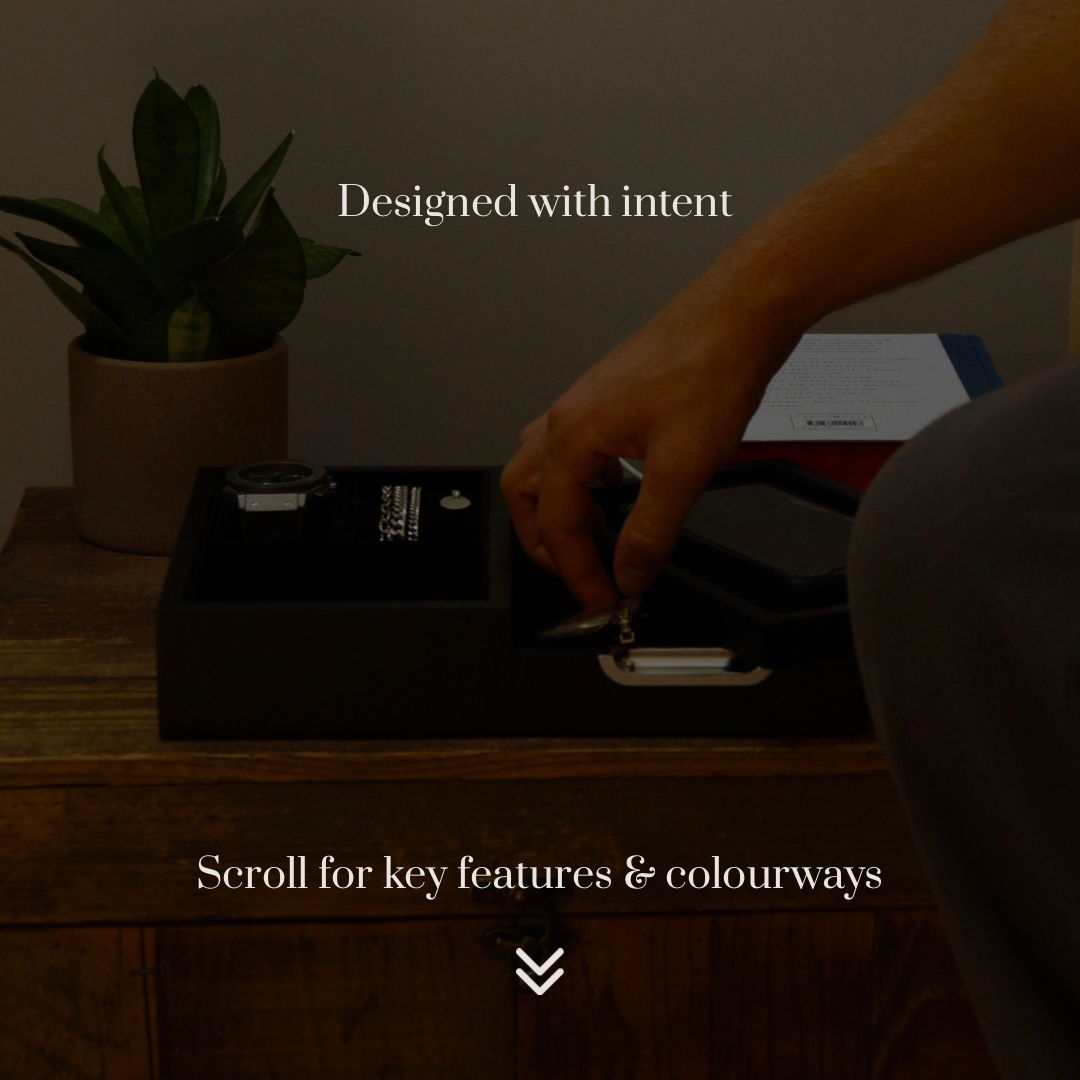 Lifestyle image of the black LDN II men’s watch, jewellery and accessory organiser by Transform on a bedside table, filled with accessories, as a man removes a pair of glasses. Darker background with text overlay reading ‘Designed with intent. Scroll for key features and colourways.