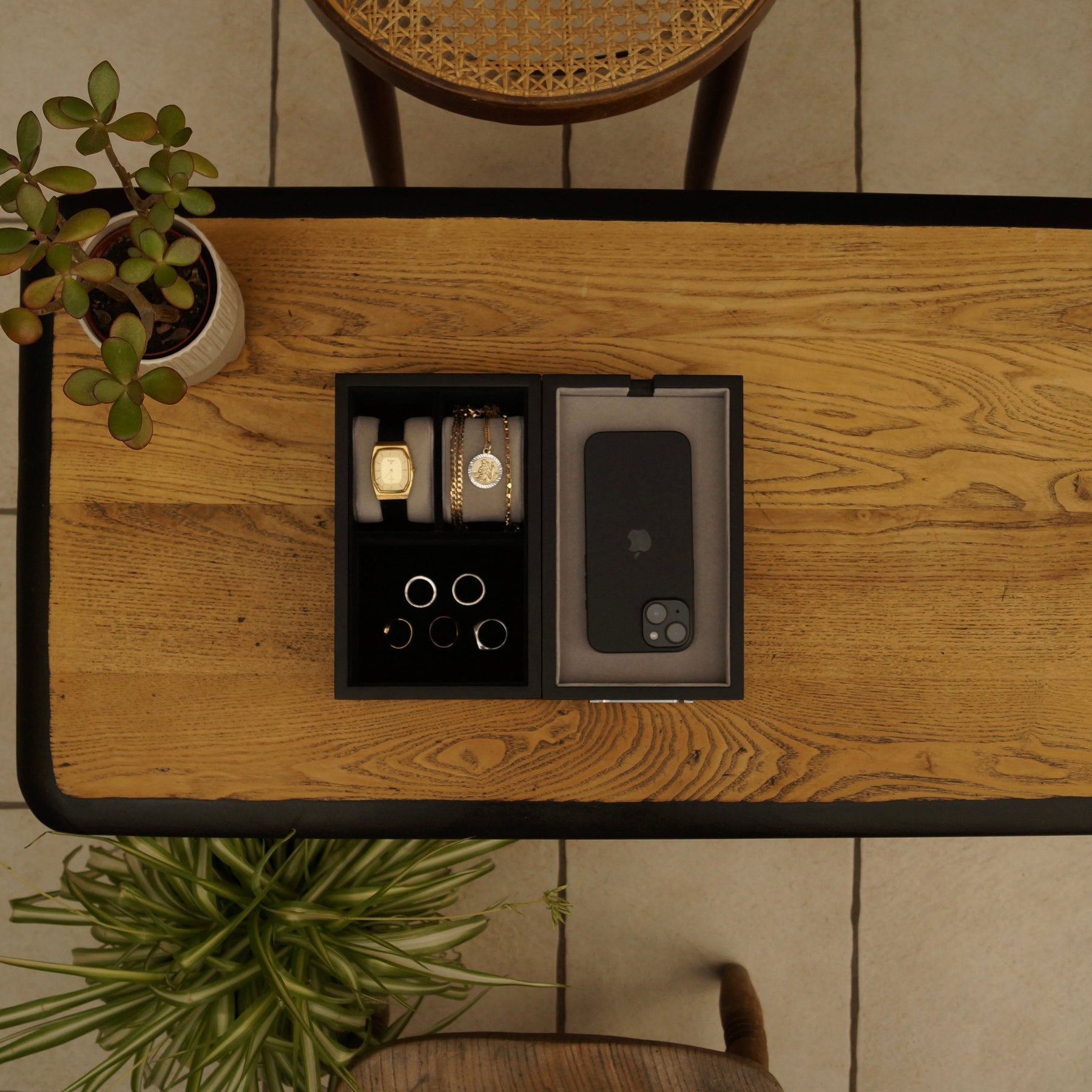 Black LDN II men’s watch, jewellery and accessory organiser by Transform in a bird’s eye lifestyle view, shown on a table with chairs and plants in the background, filled with accessories.