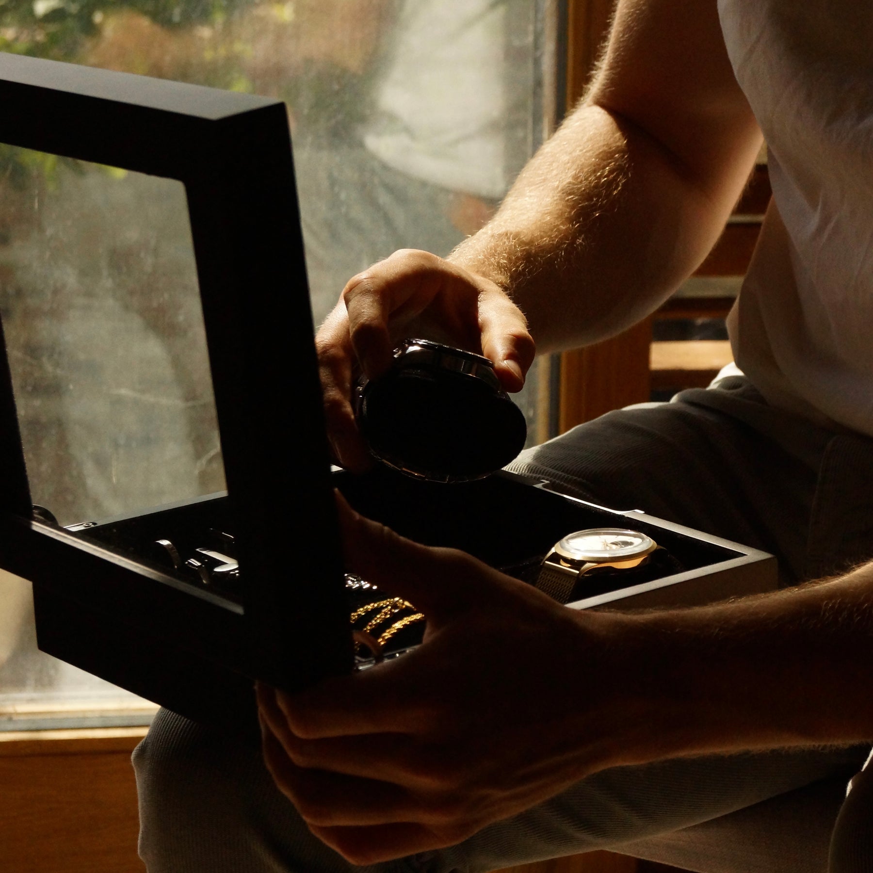 Side-on lifestyle action view of the LDN IV men’s 4-slot black watch box by Transform, as a man removes a watch from the organiser, which is also filled with other watches and jewellery.