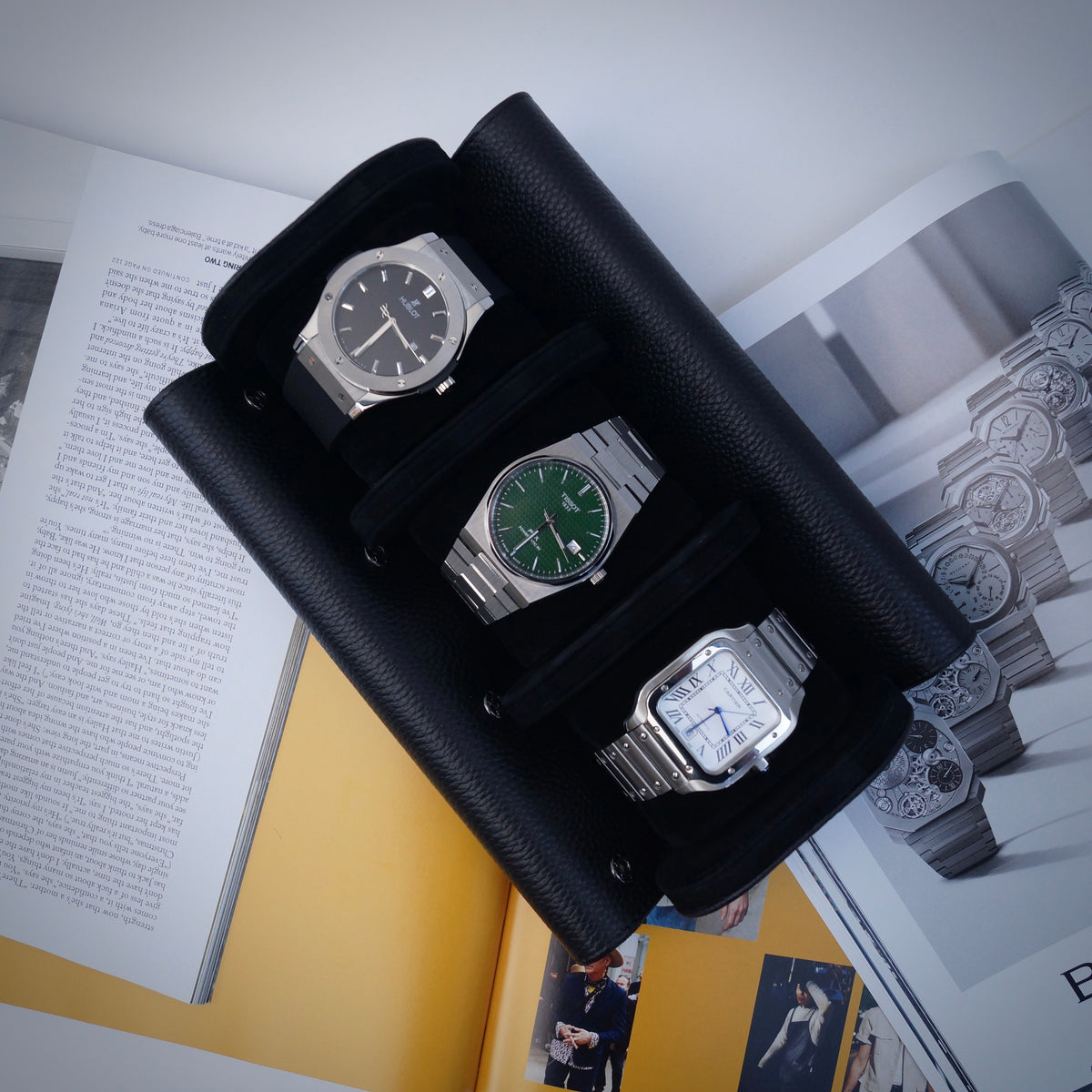 Three watches inside a black leather watch roll on a magazine background.
