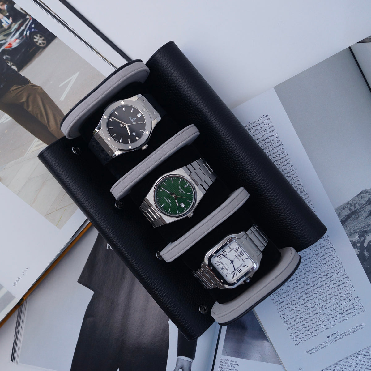 Three watches inside a black and grey leather watch roll on a magazine.