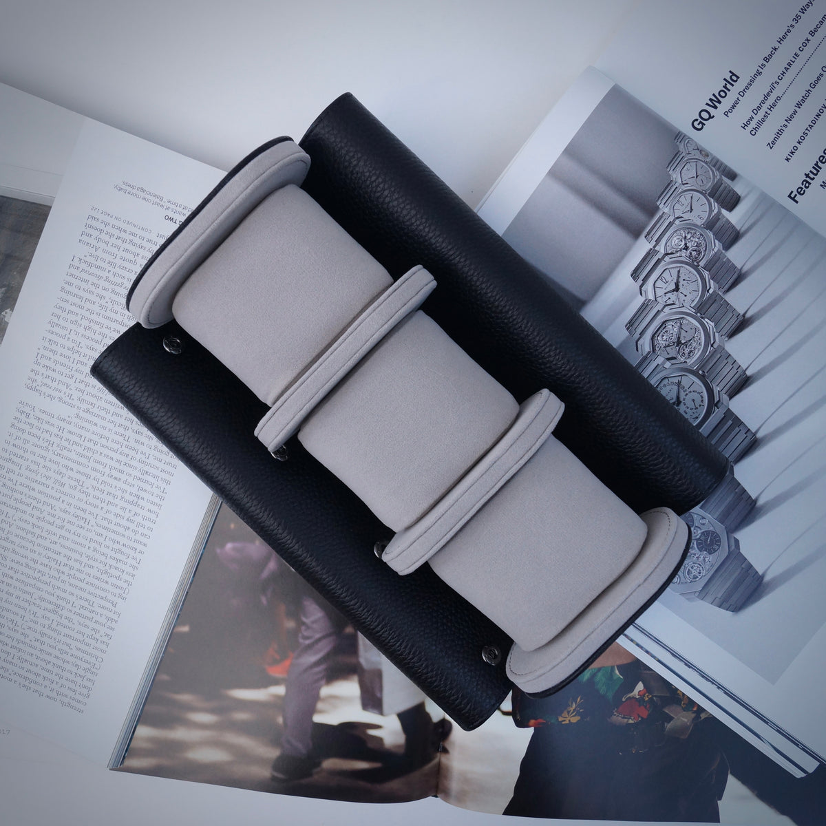 Black and grey watch roll open on top of magazines.