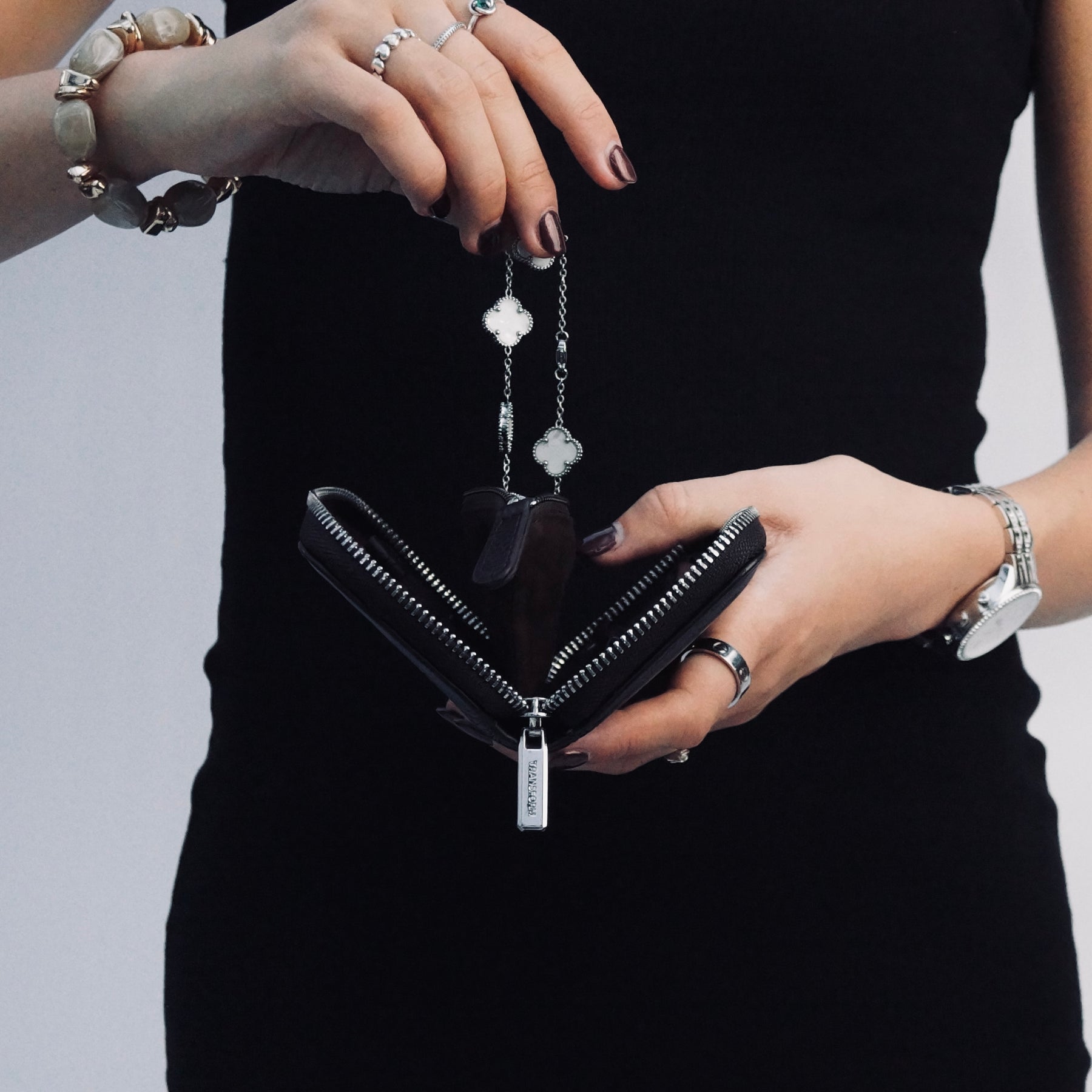 A close-up of a person putting a bracelet into a black leather jewellery case. The person is wearing a black sleeveless top and silver jewellery, including rings, bracelets, and a watch.
