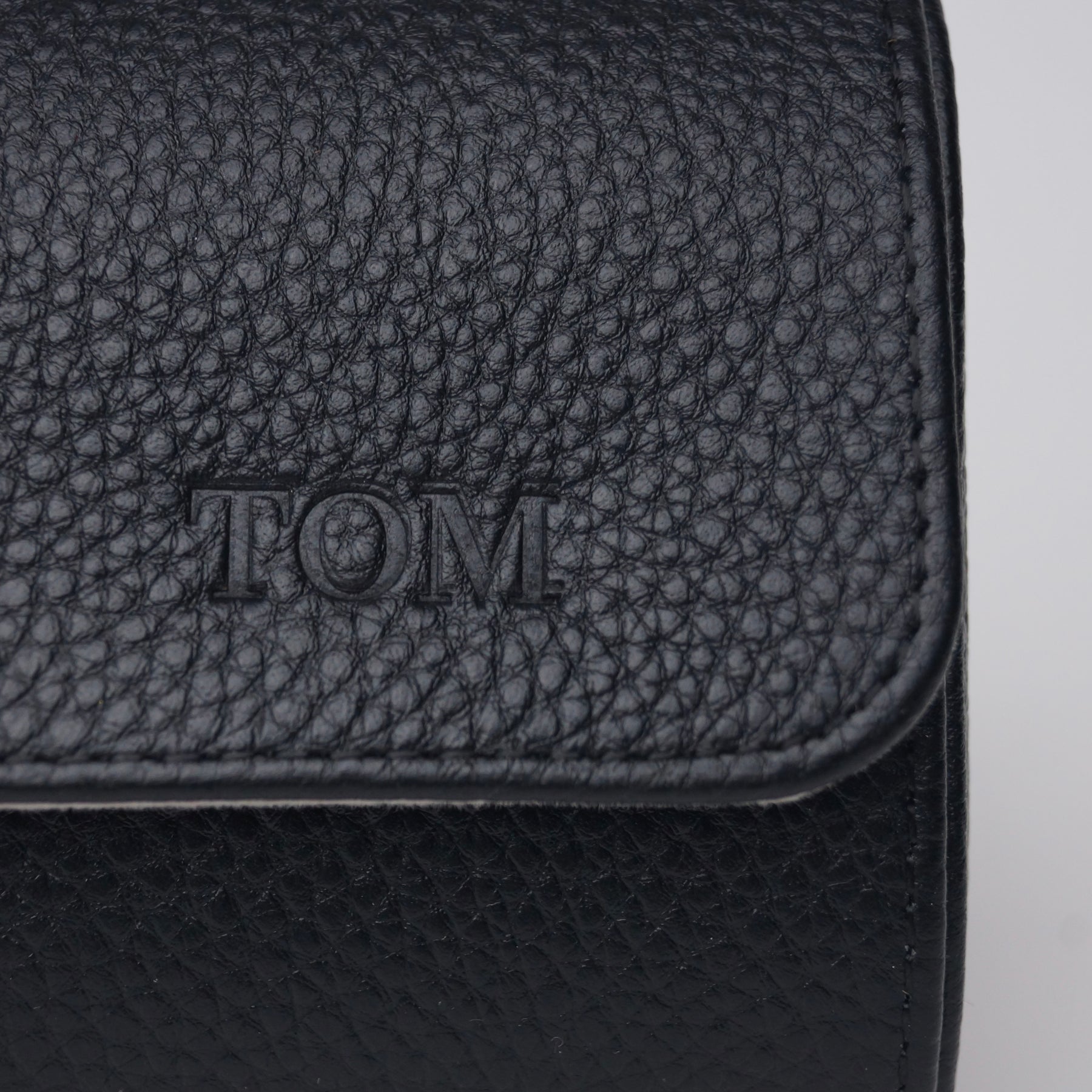Close-up of a black leather watch roll with 'Tom" engraved into the leather.