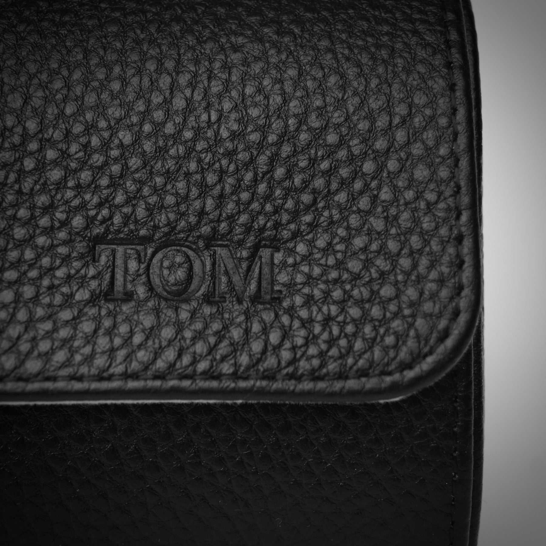Close-up of a personalised black leather watch roll with ‘TOM’ debossed into the leather.