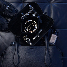 Various pieces of jewellery inside a large jewellery case sat on a handbag.