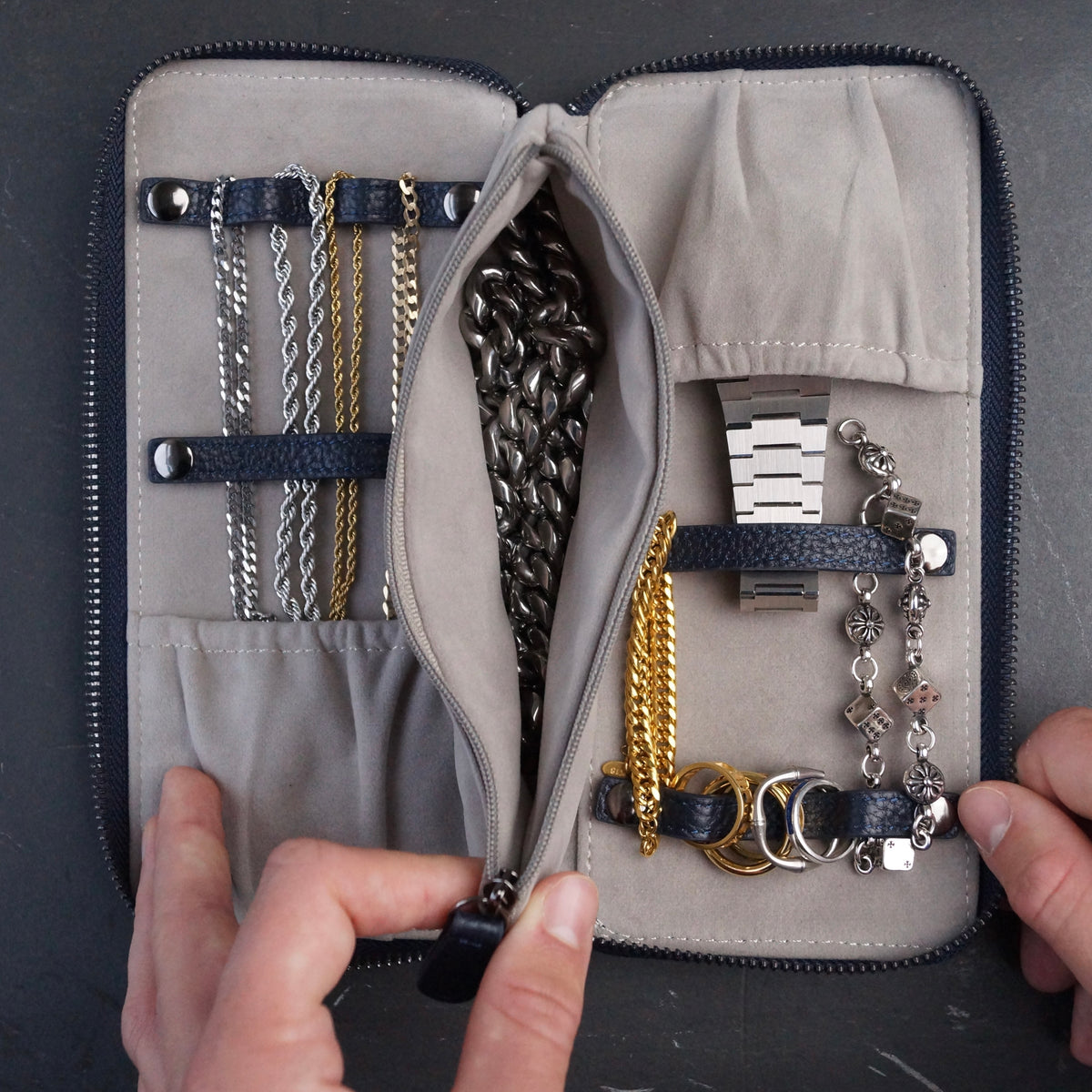 Various pieces of jewellery and a watch inside a navy and grey leather travel case.