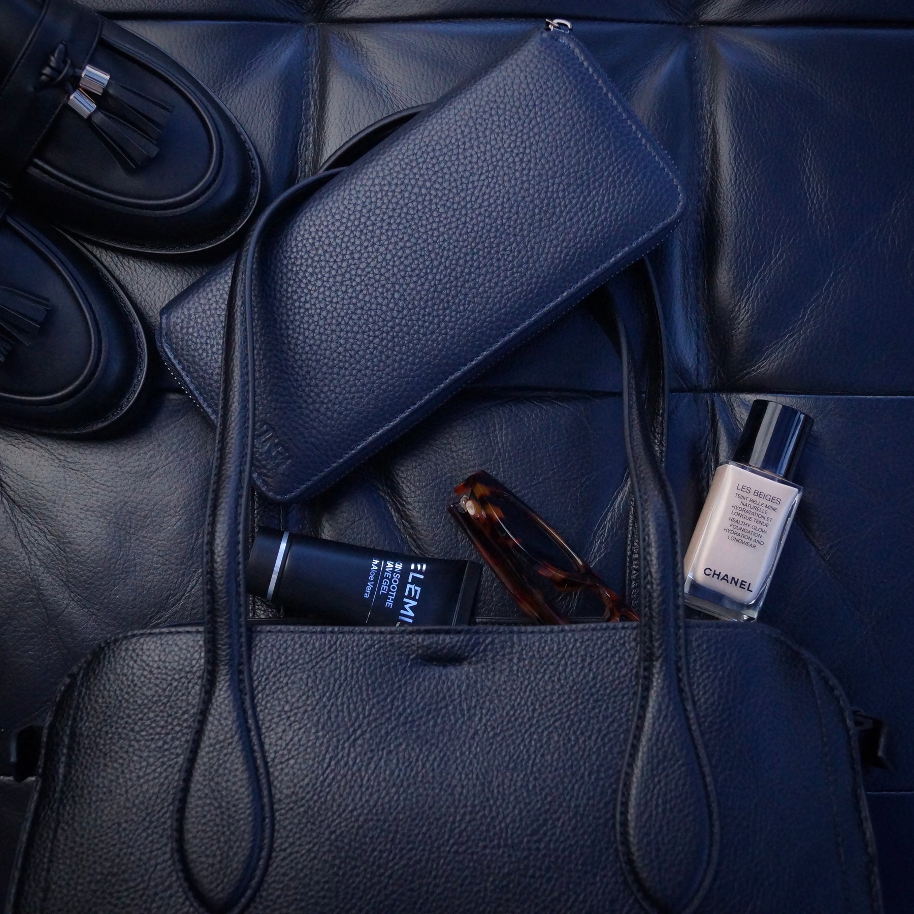 Navy blue jewellery case with a handbag and other daily essentials in the background.