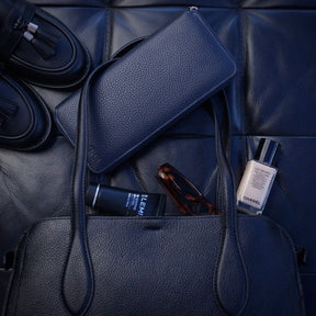 Navy blue jewellery case with a handbag and other daily essentials in the background.