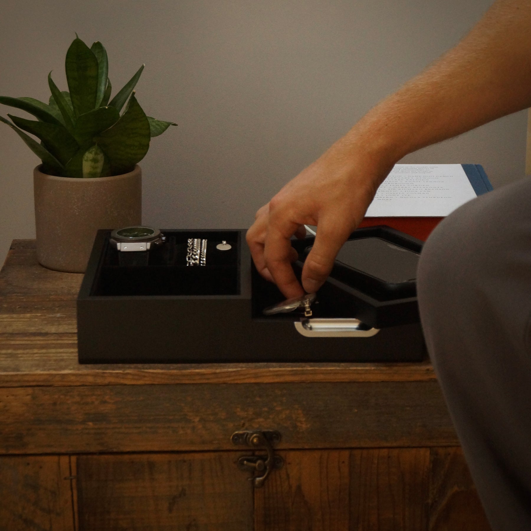 Person organising items in a jewellery box on a wooden surface with a plant in the background.