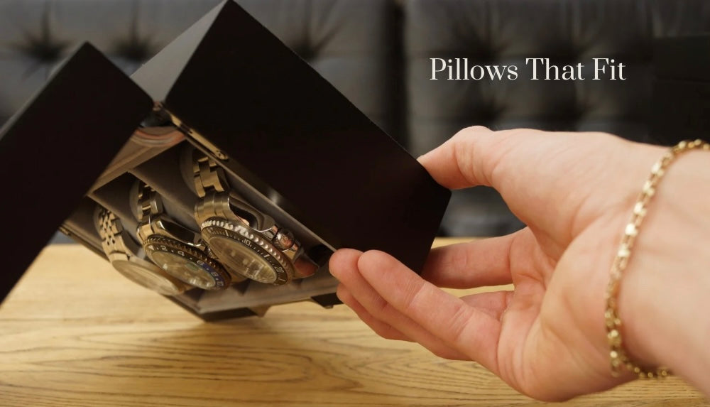 Feature demonstration image of the LDN Ill men's 3-slot black watch box by Transform, shown being held upside down by a man while filled with watches, to display how the pillows fit snugly and securely in their slots. Text overlay reads 'Pillows that fit.’