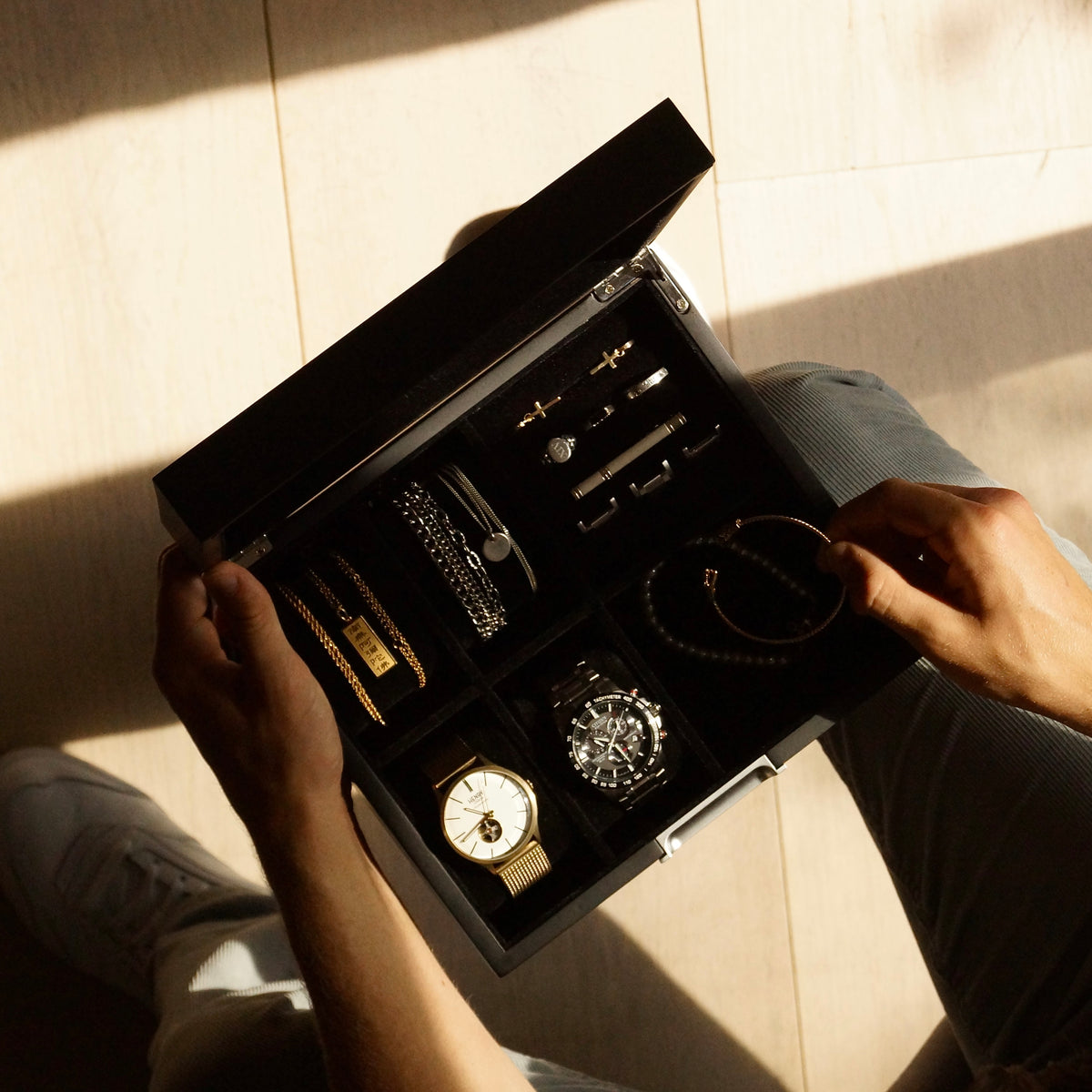 Bird’s-eye lifestyle view of the LDN IV men’s 4-slot black watch box by Transform, held by a man and filled with two watches, necklaces, bracelets, cufflinks and other accessories.