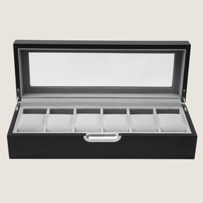 A black watch display box with an open lid and a clear glass window, showing a light grey interior with six watch slots.