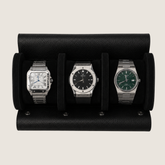 Three wristwatches displayed side-by-side in a black leather watch roll against a light beige background.