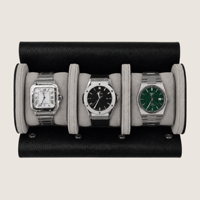 Three wristwatches displayed side by side inside a black leather watch roll with light gray fabric cushions, photographed from above on a plain light beige background.