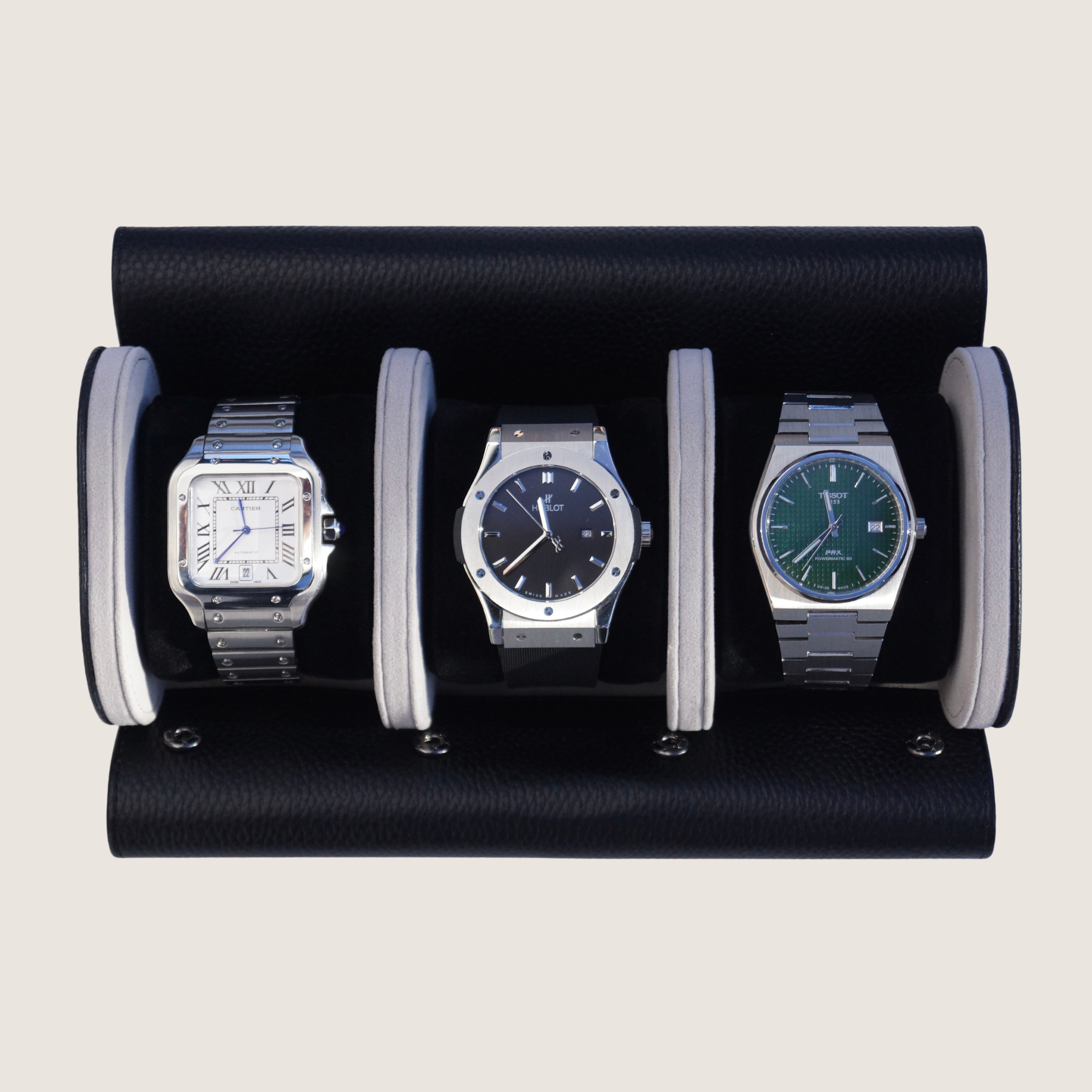 Three watches inside a black and grey leather watch roll on a beige background.