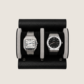 Two wristwatches displayed side by side in a black leather watch roll on a light beige background.