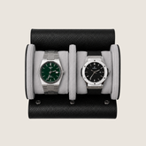 A two-watch wristwatch display stand made of black pebbled leather with light grey suede cushions.